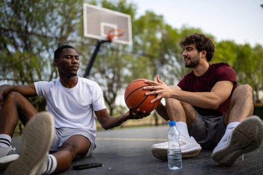 Diverse male friends resting on basketball court together