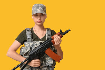 Obraz premium Confident young female soldier with assault rifle on yellow background
