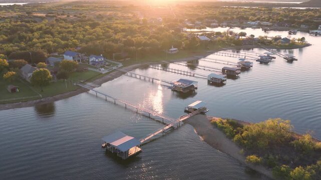 Aerial view of boathouses with docks and houses on the shore during a sunset casting golden light over the water, Possum Kingdom, Texas, United States.