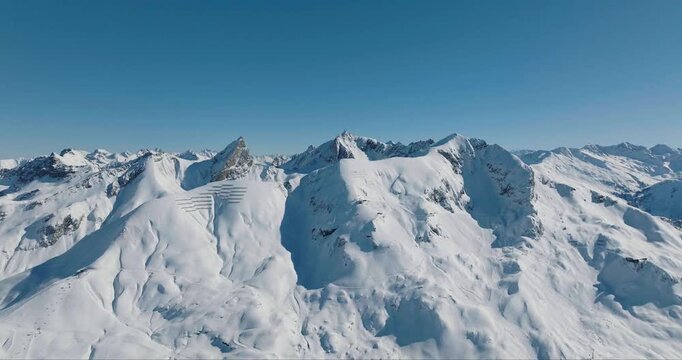 Aerial view of snow-blanketed mountain peaks glistening under a clear blue sky, a serene winter landscape, Lech, Vorarlberg, Austria.