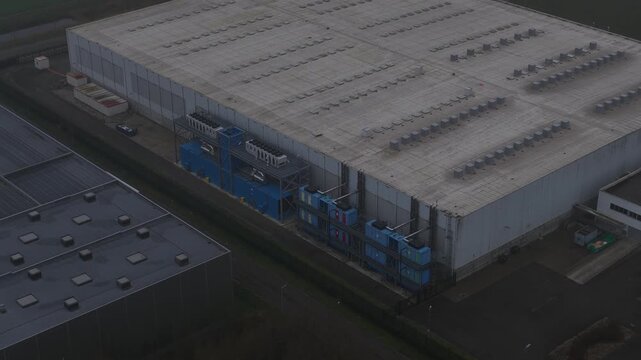 Aerial view of large industrial buildings with rooftop vents and blue structures contrasting against the grey surroundings, Roosendaal, North Brabant, Netherlands.