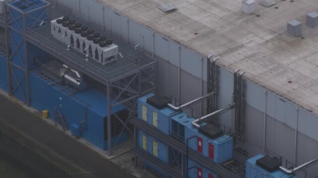 Aerial view of an industrial building with blue containers and cooling systems, showing stark geometric forms and muted tones, Roosendaal, North Brabant, Netherlands.