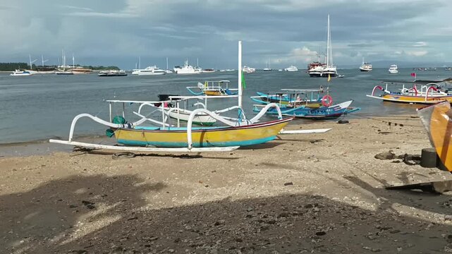 Traditional Balinese jukung fishing boats on a sandy beach under a cloudy sky