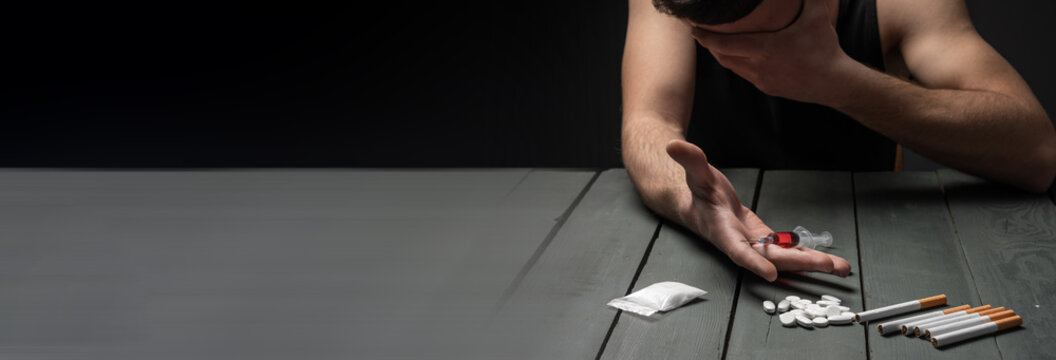 Close-up of hands holding a syringe, surrounded by scattered pills, drugs, and a cigarette, portraying substance abuse, addiction crisis, and destructive lifestyle consequences.