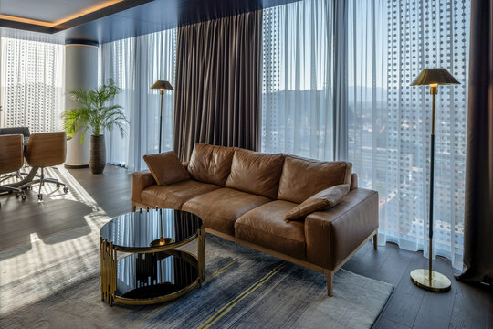 Modern living room interior with leather sofa, floor-to-ceiling windows, city view and elegant minimalist decor