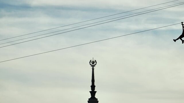 Person ziplining across sky, adventure sport with urban landmark visible below