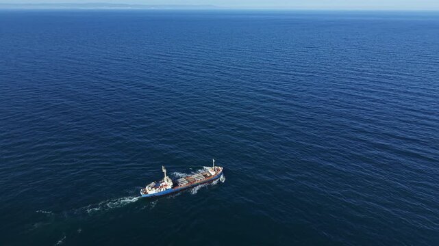 A boat travels across a vast area of blue ocean water under a clear sky. The scene shows no land, emphasizing the openness of the sea and the journey of the boat.