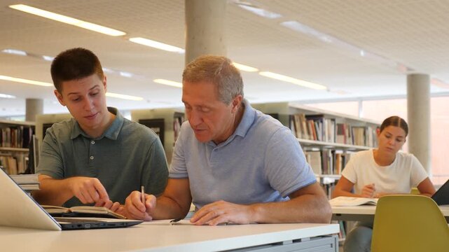  Young European man tutoring a mature Caucasian male in the library