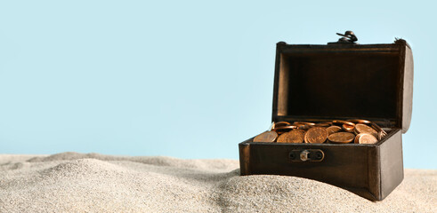 Old chest with coins on sand against blue background © Pixel-Shot