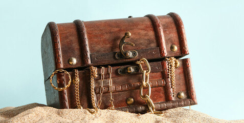 Old chest with treasures on sand against blue background © Pixel-Shot