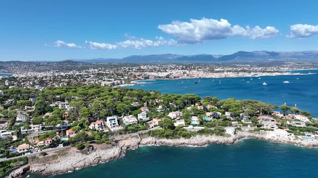 Aerial view of the stunning Antibes coastline, contrasting vibrant green trees with the deep blue sea dotted with white boats, Antibes, France.