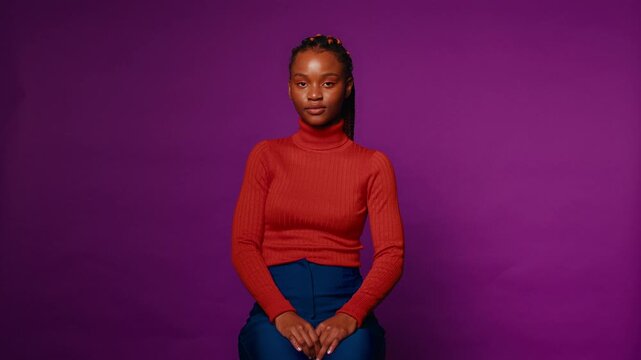 Young woman sits against a vibrant violet backdrop, her serene expression conveying confidence and composure, in this medium close-up studio shot