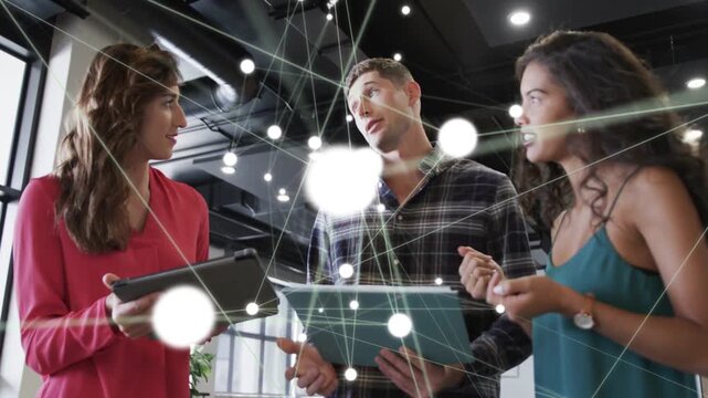 Colleagues standing and discussing while referencing tablets with network overlay in modern office