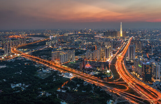 Aerial view of highways glow like fiery arteries through the urban sprawl towards the Landmark 81 skyscraper, Ho Chi Minh City, Vietnam.