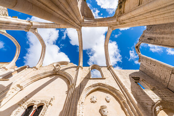 Obraz premium Dramatic upward perspective of Carmo Convent ruins in Lisbon with gothic arches and columns framing blue sky, highlighting historic architecture and open roof structure.