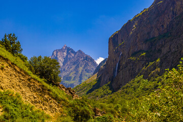 Obraz premium Majestic mountain peaks with waterfall in lush valley
