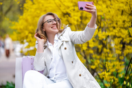 Woman taking selfie on bench with shopping bags. Spring mood and happy lifestyle.
