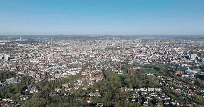 Aerial view of urban buildings and lush green trees blending with the city's landscape under a clear blue sky, Nancy, France.