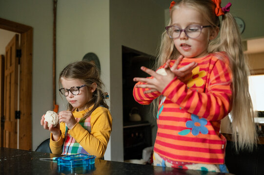 Sisters rolling pastry at the kitchen table while baking as a family, looking concentrated