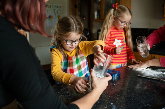 Mother and daughters rolling out pastry with glasses and spreading flour on the table