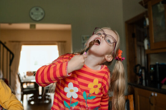 Child sticking knife full of chocolate spread in her mouth while baking