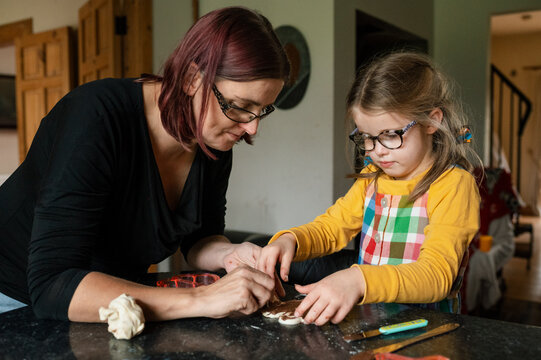 Mother and daughter spreading chocolate spread on heart shaped pastry in their kitchen