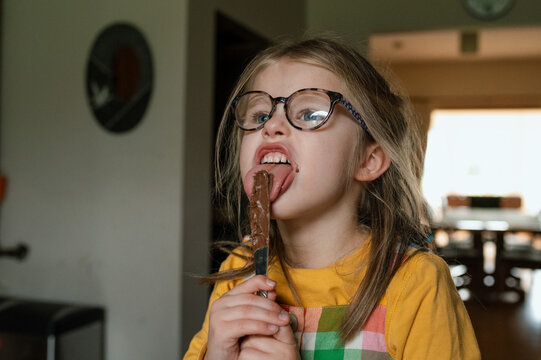 Child with glasses licking chocolate spread off a knife