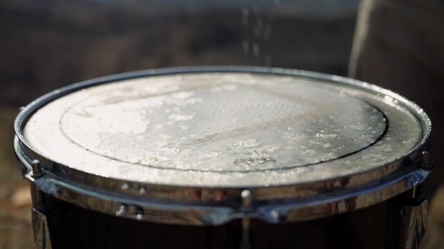 Slow motion drum being struck as water splashes dramatically on the drumhead impact