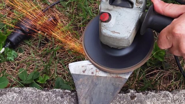 Close-up of men's hands sharpening an axe on an electric sharpener. Repair of home tools. Sparks fly. Close-up of a man sharpening an axe with a grinder