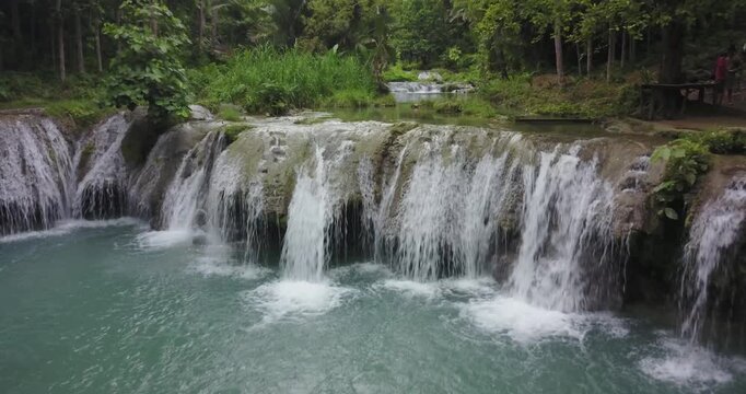Drone shot descending towards tropical waterfall and natural pool in lush jungle, ending close to falling water in Siquijor, Philippines