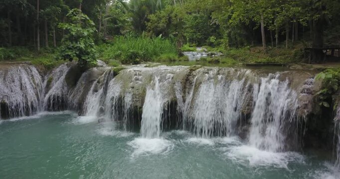 Drone shot flying forward towards tropical waterfall and natural pool surrounded by lush jungle in Siquijor, Philippines