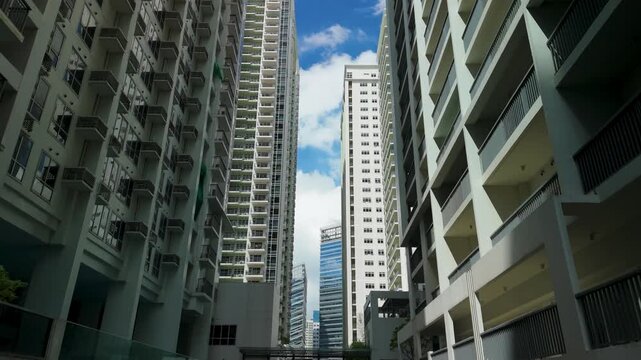 Drone rises through narrow urban canyon between modern high-rise condominium towers in Bonifacio Global City revealing blue sky above balconies