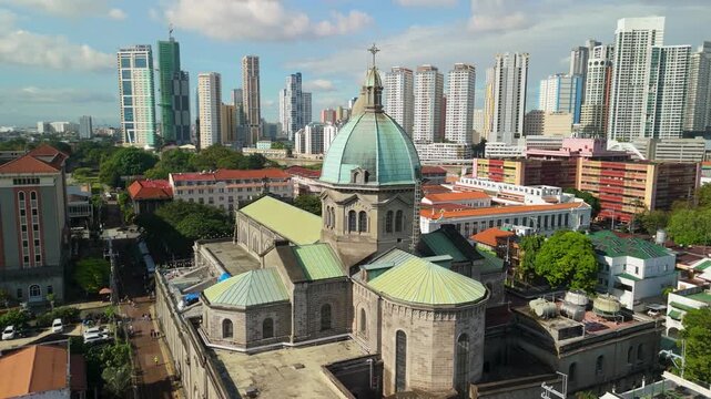 Drone circles majestic Manila Cathedral showing neo romanesque stone architecture and iconic dome with Intramuros city skyline in background during sunny day in Manila Philippines