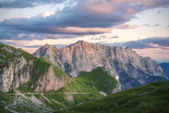 Aerial view of the majestic Mangart mountain range, its rugged peaks kissed by the soft glow of the setting sun, casting shadows across the verdant valleys below, Log pod Mangartom, Bovec, Slovenia.