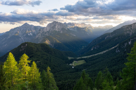 Aerial view of the dramatic, sun-kissed Mangart mountain range and the lush green valley below create a breathtaking landscape, Log pod Mangartom, Bovec, Slovenia.