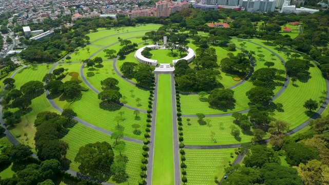Wide cinematic drone tilt movement revealing the vast green grounds and white marble crosses of the Manila American Cemetery and Memorial with the urban skyline in the background