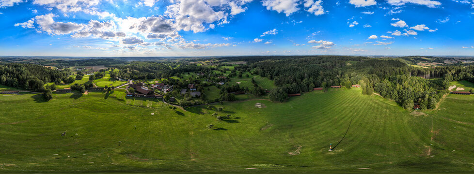Aerial view of lush green meadows meeting dense forests under a bright blue sky dotted with puffy clouds, Bad Griesbach, Germany.