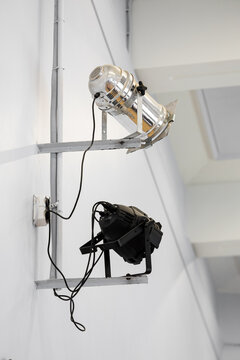 Two mounted stage spotlights, one metallic and one black, fixed on brackets against a white wall with visible cables, creating a clean industrial look with ample copy space