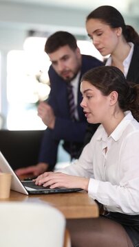 Group of man and women colleagues discussing around laptop at office table 