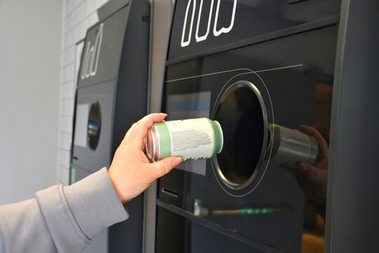 Returning empty cans to a supermarket recycling machine to reduce waste and reuse aluminum.A woman throws an aluminum can into a recycling machine.