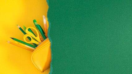 Naklejka premium Back to school concept with yellow pencil case full of stationery under torn green paper on yellow background, minimalist creative flat lay with copy space for text, education and study banner.