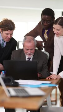 Group of colleagues look at laptop screen and laugh, video chat with clients or customers, casual communication. Atmosphere of corporate work, active working day, active team