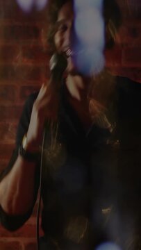 Vertical video: Male singer gripping mic cord singing in music bar as lens flares hiding face