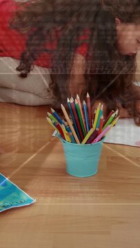 Two girls leaning toward blue painting, first reaching red pencil from turquoise cup, creating art