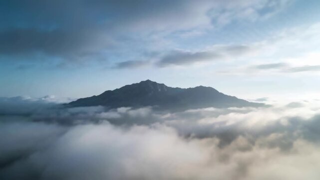 Drone moving forward right, parting cloud bank and revealing mountain summit at sunrise for travel