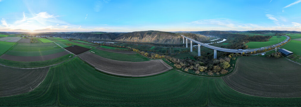 Aerial view of the Hochmoselbrucke bridge soaring over verdant fields and the winding Moselle River under a bright sky, Dieblich, Germany.