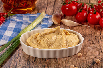 Fototapeta premium Creamy hummus dip in white bowl, fresh tomatoes, garlic, green onion, olive oil, chickpeas on rustic wood background
