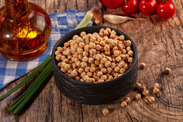 Fototapeta premium Dry chickpeas in black bowl with fresh ingredients on rustic wood
