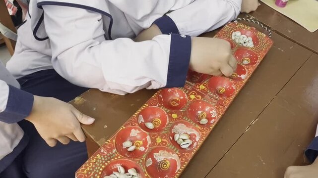 School Students Playing Traditional Congklak Mancala Board Game At Classroom Desk