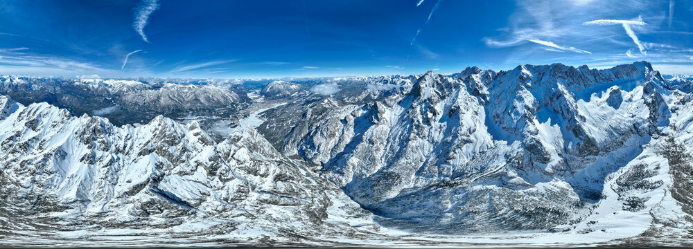 Aerial view of snow-capped mountains pierce the crisp, clear blue sky, casting long shadows over the serene valley below, Garmisch-Patenkirchen, Bavaria, Germany.